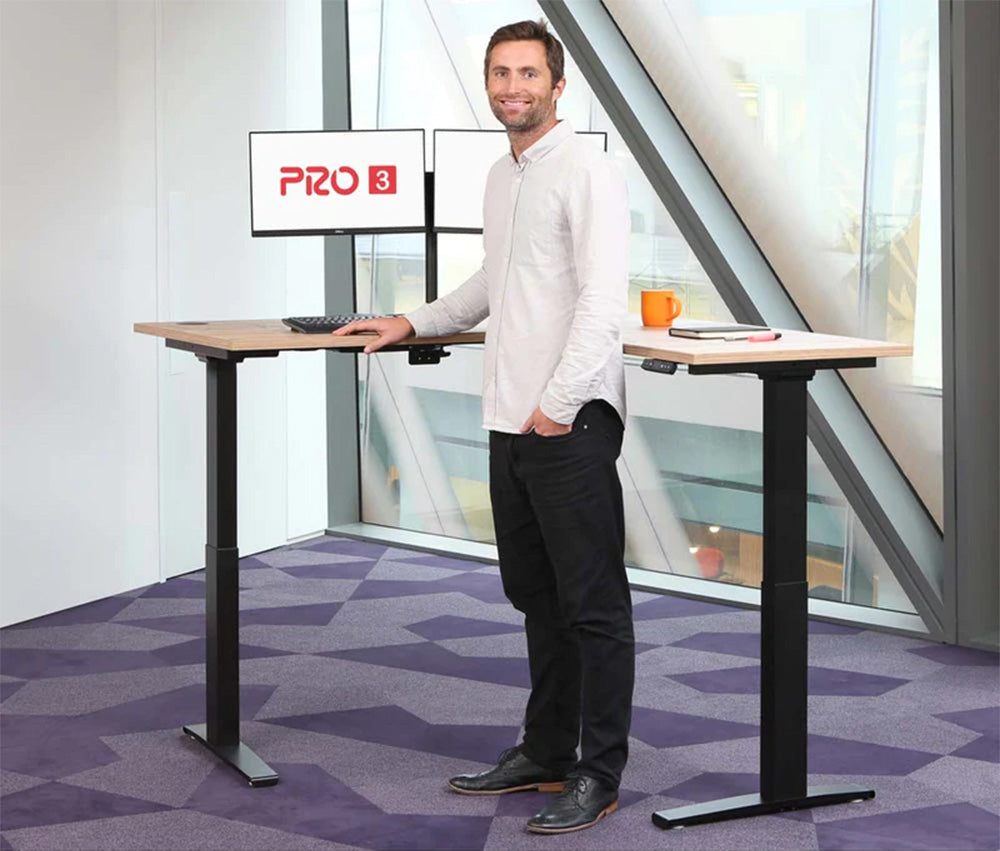 An L-shaped corner sit-stand desk with a pale top and a black three-legged frame.