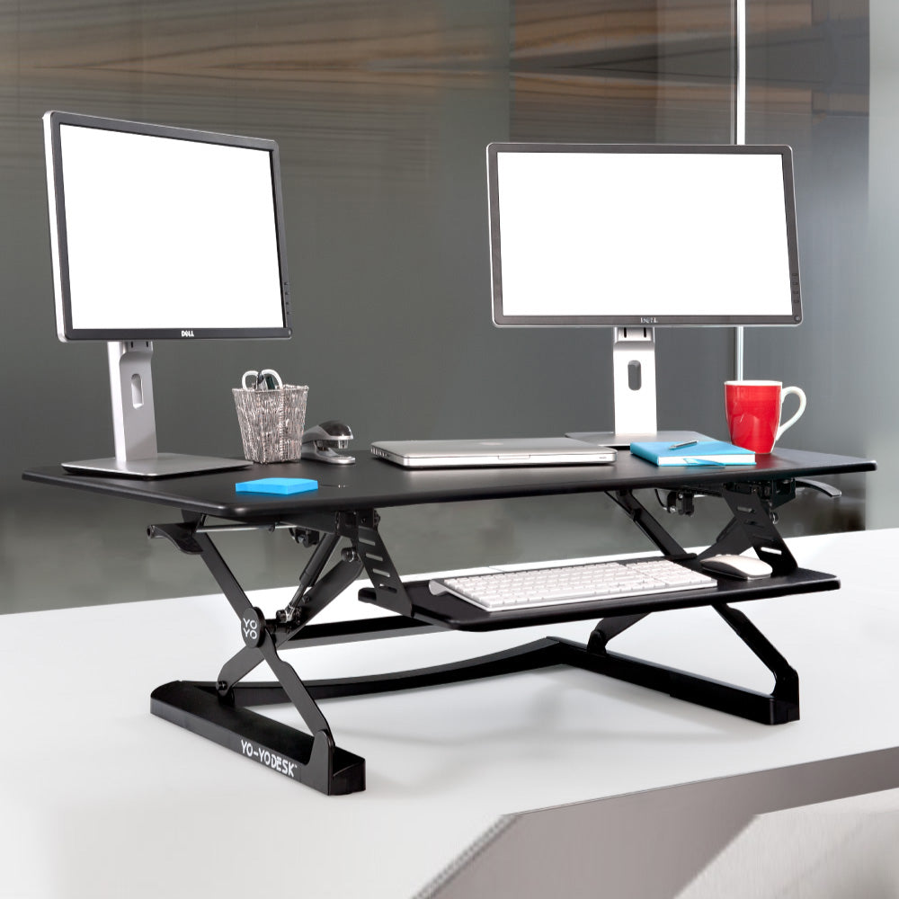 A wide black desk riser with a worktop above and a separate keyboard tray below.
